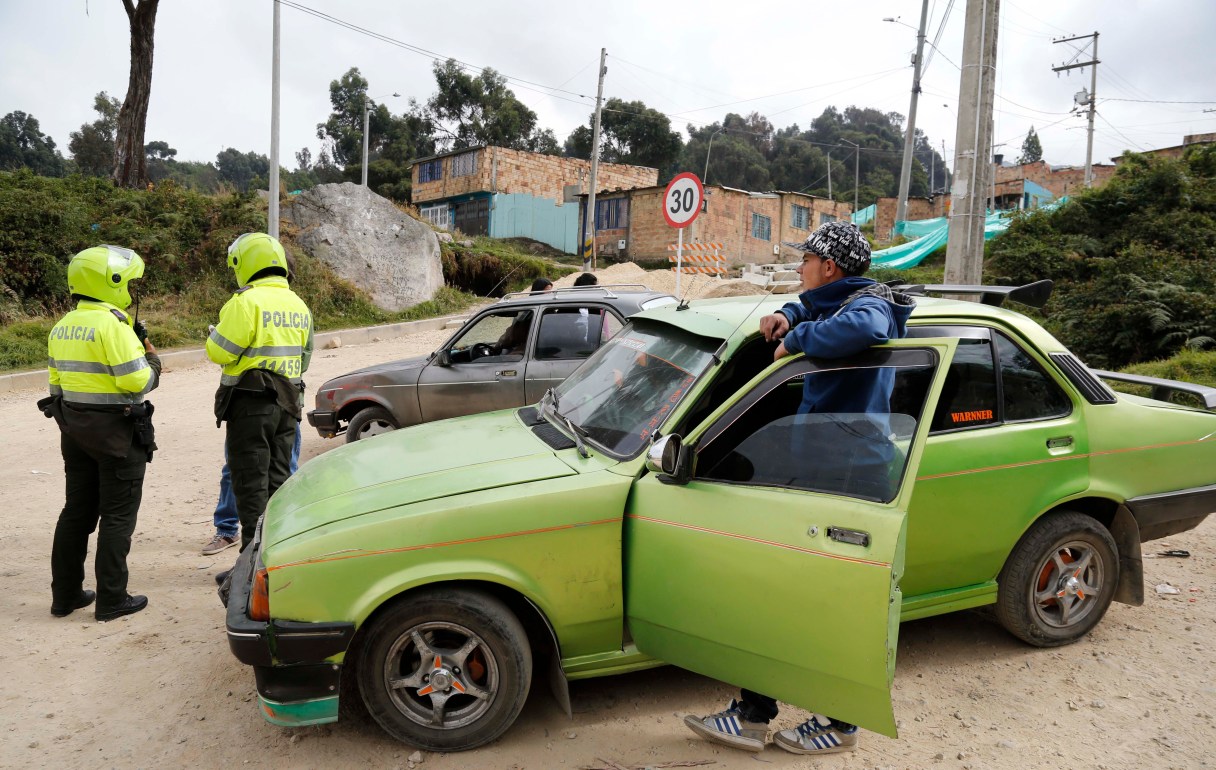 In this Jan. 15, 2015 photo, police check the ID's of unlicensed cabbies in Usme, on the outskirts of Bogota, Colombia. In Usme, unlicensed cabbies eke out a living shuttling residents up steep dirt roads where buses and regular taxis won’t venture. For years each driver was forced to fork over about half their earnings to appease extortionists, but the criminal ring was dismantled in 2014 after a desperate cabbie secretly went to Colombia’s elite Gaula police unit. (AP Photo/Fernando Vergara)