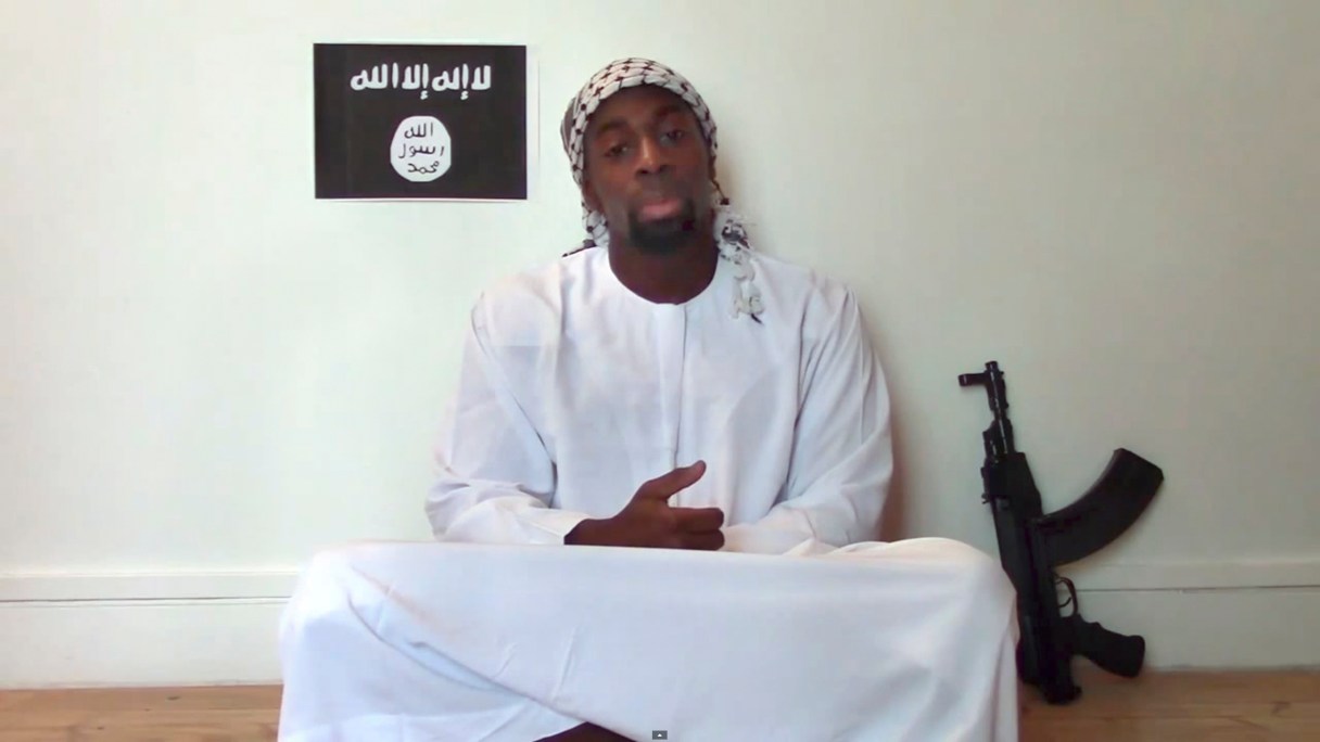 FILE - This Jan.11, 2015, file image made from a video posted online by militants shows slain hostage-taker Amedy Coulibaly, who shot a policewoman and four hostages at a kosher grocery in Paris, with a gun in front of an Islamic State emblem as he defends the Paris attacks carried out on the satirical newspaper, police and a Jewish store. Police and security officials say four people are in custody over links to three days of attacks that terrorized Paris this year, including a policewoman in a relationship with one of the others. The officials, who spoke on condition of anonymity because the investigation was ongoing, said one of the men detained had ties to Amedy Coulibaly. No one has been linked directly to the Jan. 7-9 attacks at the satirical newspaper Charlie Hebdo and the market, which left a total of 20 people dead, including all three gunmen. (AP Photo/Militant Video, File)