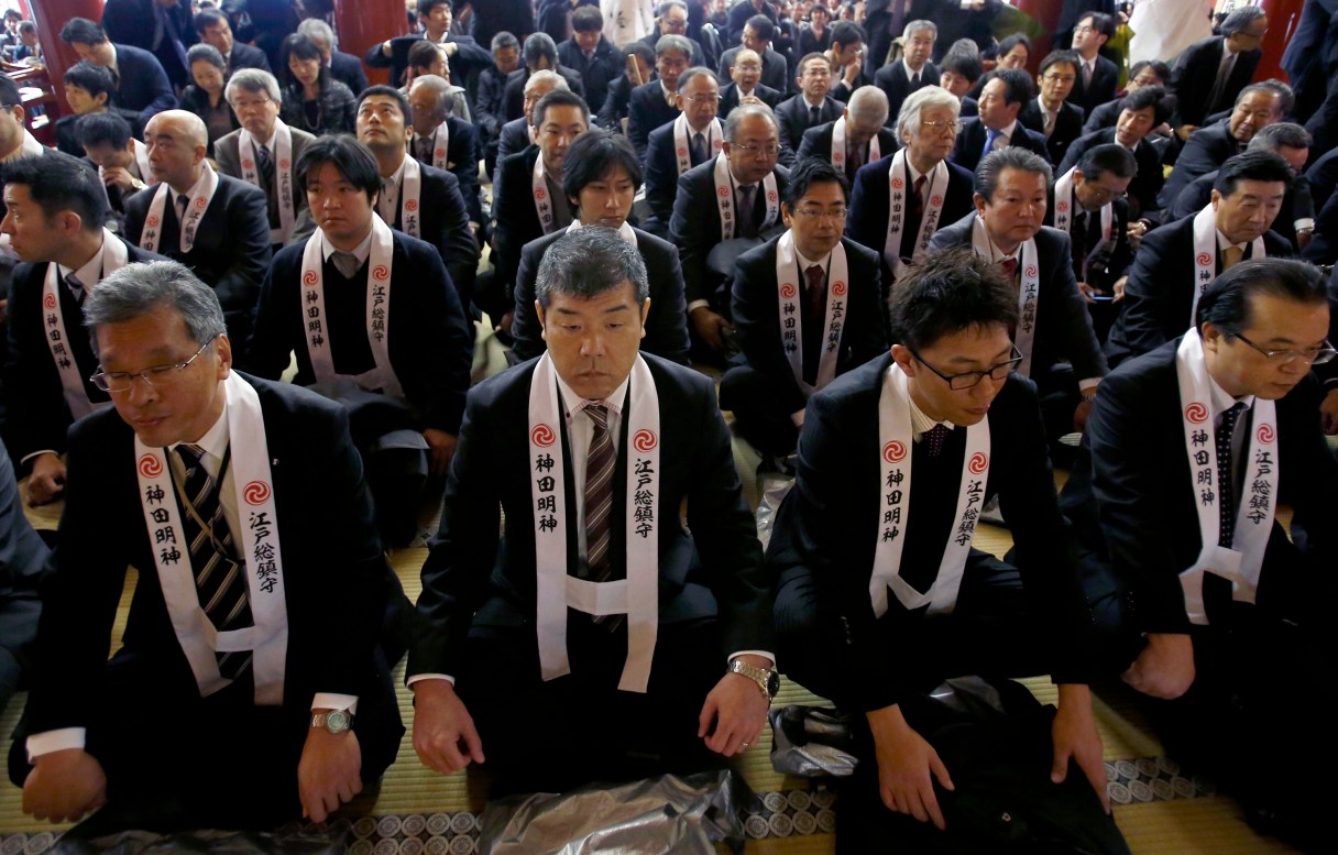 FILE - In this Jan. 5, 2015 file photo, company workers are seated on the main hall of Kanda Myojin shrine, known as the shrine of commerce and industry, as they offer prayers for a good business year on the first business day of the year. Japan’s future prosperity will depend on improving its lagging productivity, says a report by McKinsey Global Institute that urges companies to boost their own competitiveness by better use of their workers. The report suggests better use of women and older workers; improved access to financing for entrepreneurs, and a more aggressive approach to tackling global markets by making company management more global in nature. (AP Photo/Shizuo Kambayashi, File)