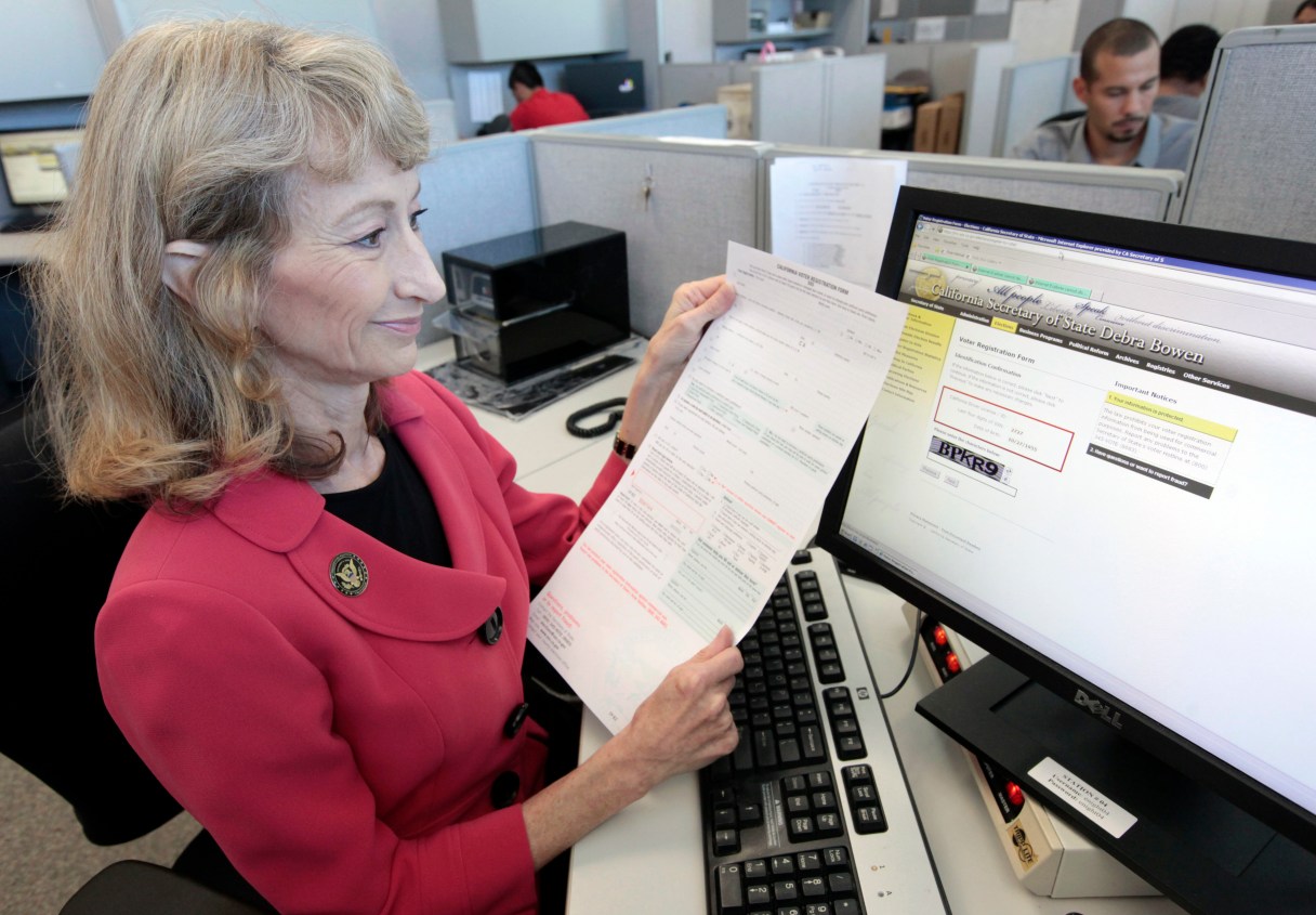 FILE - In this Sept. 19, 2012 file photo, then-California Secretary of State Debra Bowen, shows a online voter registration system as she holds a traditional written form in Sacramento, Calif. Applicants can fill out a form online that will be checked against their driver's license or the state identification card held by the California Department of Motor Vehicles. When President Barack Obama was first elected in 2008, only two states offered an online website where citizens could register to vote. Five states now allow citizens without a state identification or driver’s license to register to vote online: California, Delaware, Minnesota, Missouri, and Virginia. (AP Photo/Rich Pedroncelli, File)