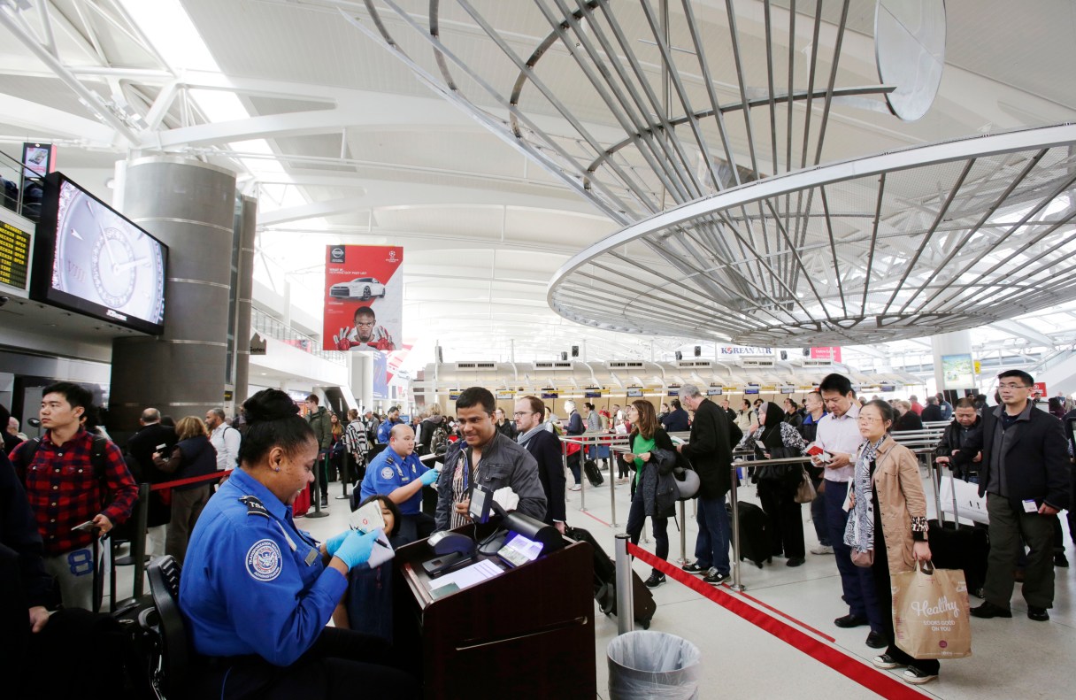FILE - In this Oct. 30, 2014, file photo, a TSA officer, left, checks a passenger's ticket, boarding pass and passport as part of security screening at John F. Kennedy International Airport in New York. A court challenge over the difficulty for airline passengers to remove their names from the U.S. government’s no-fly list is taking an unexpected twist, now focusing on the mysterious ways federal agents add passenger names to the list in the first place. (AP Photo/Mark Lennihan, File)