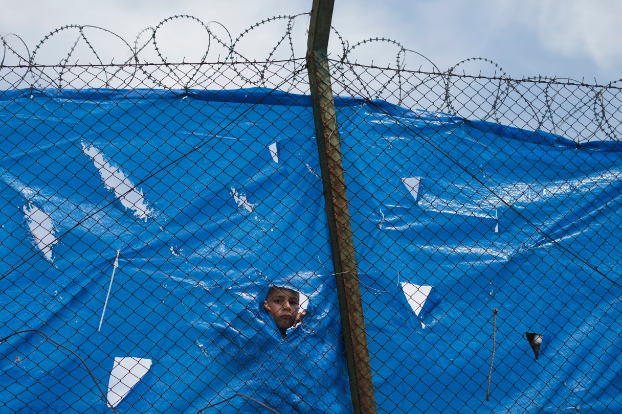 An Afghan child looks out behind a wire fence of a refugee camp in the western Athens' suburb of Schisto, Monday, March 28, 2016. The camp is hosting 1971 people most of them from Afghanistan as around 50,000 refugees and migrants are stuck in Greece. (AP Photo/Petros Giannakouris)