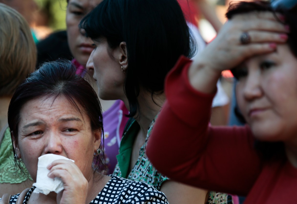 Colleagues and relatives of dead workers from Kyrgyzstan react as they gather next to the burnt building of a printing plant's warehouse in Moscow, Russia, Saturday, Aug. 27, 2016. Russian emergency services say a fire swept through a printing plant's warehouse in Moscow on Saturday, killing 17 migrant workers from Kyrgyzstan. (AP Photo/Ivan Sekretarev)