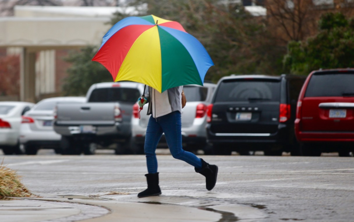 A pedestrian shields herself from freezing rain in downtown Bartlesville, Okla., Friday, Jan. 13, 2017. An ice storm is expected to hit the area today. A winter storm that pounded northern California is descending upon the southern Plains, packing crippling ice accumulations and heavy rain that could cause widespread power outages and flooding. (Mike Simons/Tulsa World via AP)