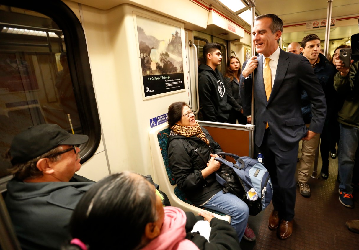 FILE - In this Dec. 6, 2016, file photo, Los Angels Mayor Eric Garcetti, right, talks to passengers aboard a Metro Red Line train that he boarded at the Universal City Red Line station in Los Angeles. Garcetti's toughest competitor in his campaign for a second term might not be another candidate. The mayor shares the ballot with a proposal intended to restrict large real estate projects that challenges his vision for building thousands of new apartments clustered around train stations. (Al Seib/Los Angeles Times via AP, Pool, File)
