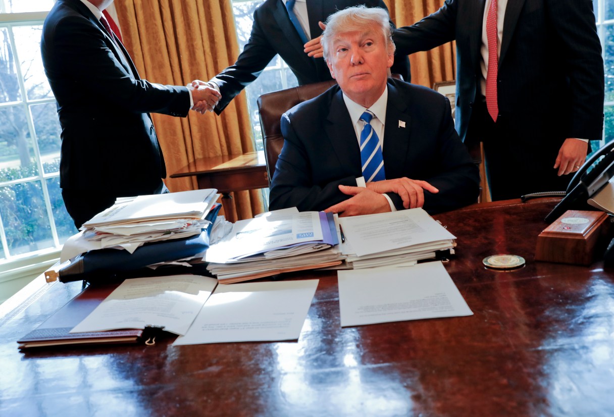 President Donald Trump sits at his desk after a meeting with Intel CEO Brian Krzanich, left, and members of his staff in the Oval Office of the White House in Washington, Wednesday, Feb. 8, 2017. (AP Photo/Pablo Martinez Monsivais)