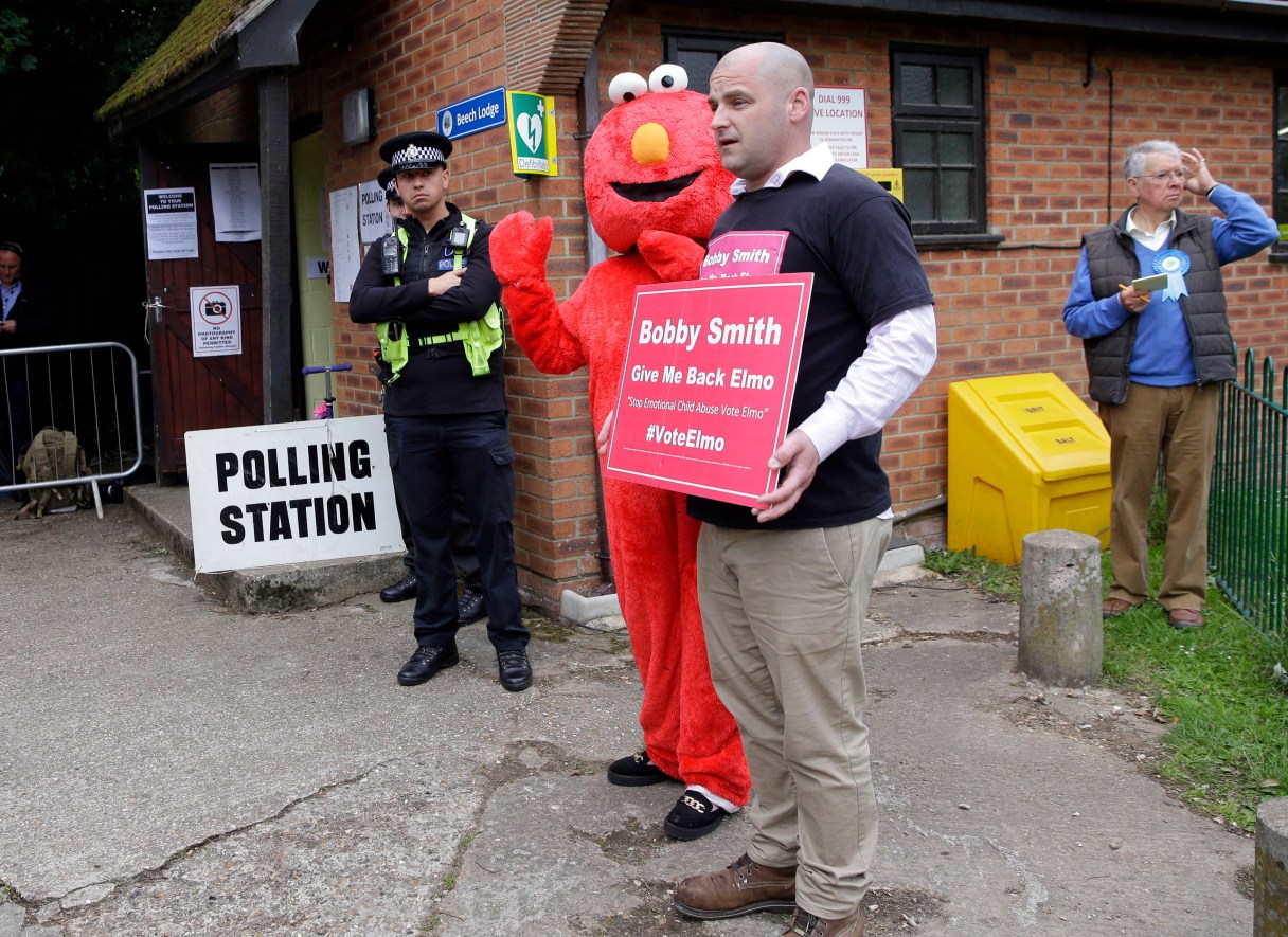 British political and fathers' rights activist, Bobby Smith stands alongside a person wearing a costume of childrens' TV character Elmo, outside a polling station in Maidenhead, England, where Britain's Prime Minister Theresa May is due to arrive to vote in the general election Thursday, June 8, 2017. Smith is the founder and leader of the Give Me Back Elmo party. (AP Photo/Alastair Grant)