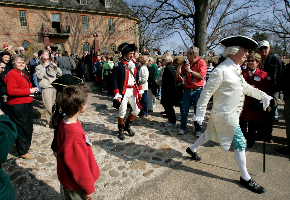 FILE - In this Friday March 18, 2006 file photo, visitors to Colonial Williamsburg gather in the courtyard of the Colonial Capital as they watch the Royal Governor played by, Stephen Moore, right, a historical interpreter in a program called "Revolutionary City" in Williamsburg, Va. Colonial Williamsburg, facing a decline in visitors and hundreds of millions in debt, announced Thursday, June 30, 2017 it will outsource many of its commercial operations in a restructuring that will include layoffs. (AP Photo/Steve Helber)