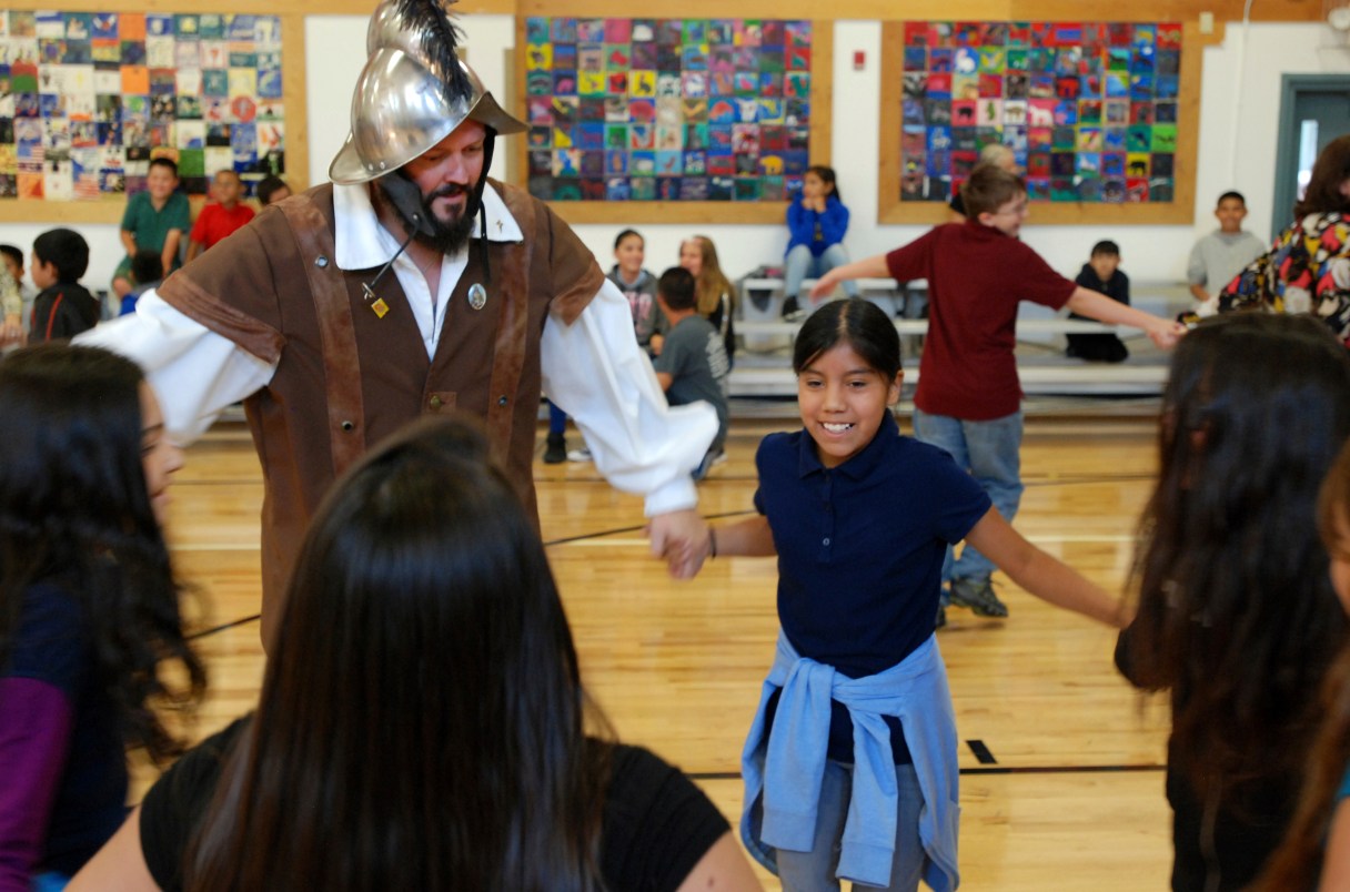 In this Wednesday, Aug. 30, 2017 photo, Edwin Quintana, left, dances with fifth grader Kaylee Pacheco and other students at Tesuque Elementary school in Tesuque, N.M. The students and others in Santa Fe's public school district were allowed to skip the annual presentation of Spanish colonial culture and history that honors a 17th century conquistador, in deference to Native American students and others who may find the performances disrespectful. None opted out in Tesuque. Public statues and tributes to early Spanish conquerors are enduring increased criticism tied to the brutal treatment of American Indians centuries ago by soldiers and missionaries. (AP Photo/Morgan Lee)