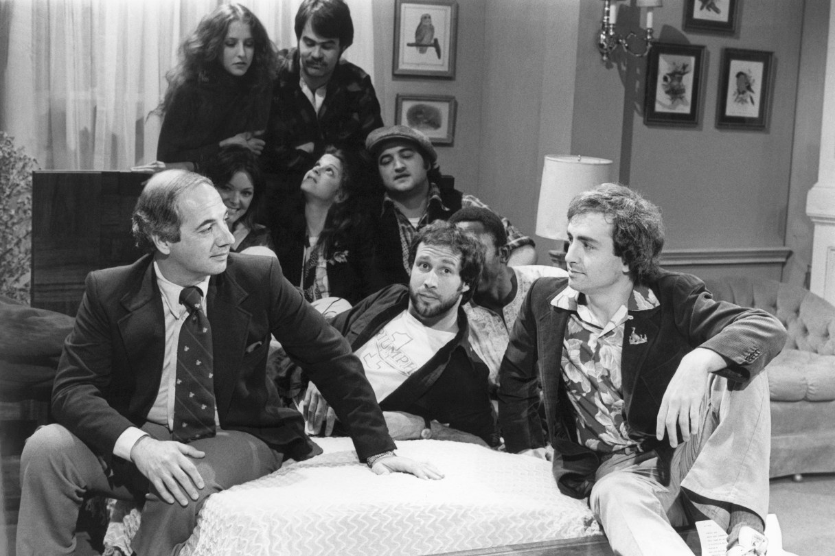 FILE - White House Press Secretary Ron Nessen, left, appears on the "Saturday Night Live" set with producer Lorne Michaels, right, and cast members Chevy Chase, foreground center, Laraine Newman, background left, Dan Aykroyd, background right, Jane Curtain, second row from left, Gilda Radner, John Belushi and Garret Morris, partially obscured, on April 17, 1976, in New York. (AP Photo)