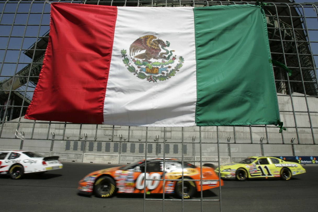 FILE - Cars drive past the flag of Mexico placed at the fence during the NASCAR Busch series auto race at the Hermanos Rodriguez racetrack in Mexico City, Mexico, on Sunday, March 5, 2006.(AP Photo/Gregory Bull, file)