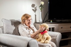 Carol DeMaio, 80, who has dementia, with her robotic dog Sabrina, named after a golden retriever who died, at her home in Garnerville, N.Y., on March 10, 2026. When DeMaio sleeps, the robot dog stays at the foot of her bed, reacting when she stirs awake.(Bryan Anselm/The New York Times)