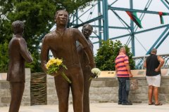 Staff photo by Olivia Ross / A couple reads about the Ed Johnson Memorial on June 10, 2022. The memorial depicts Ed Johnson and his attorneys, with flowers left by visitors. Johnson was mob-lynched from the Walnut Street Bridge in 1906.